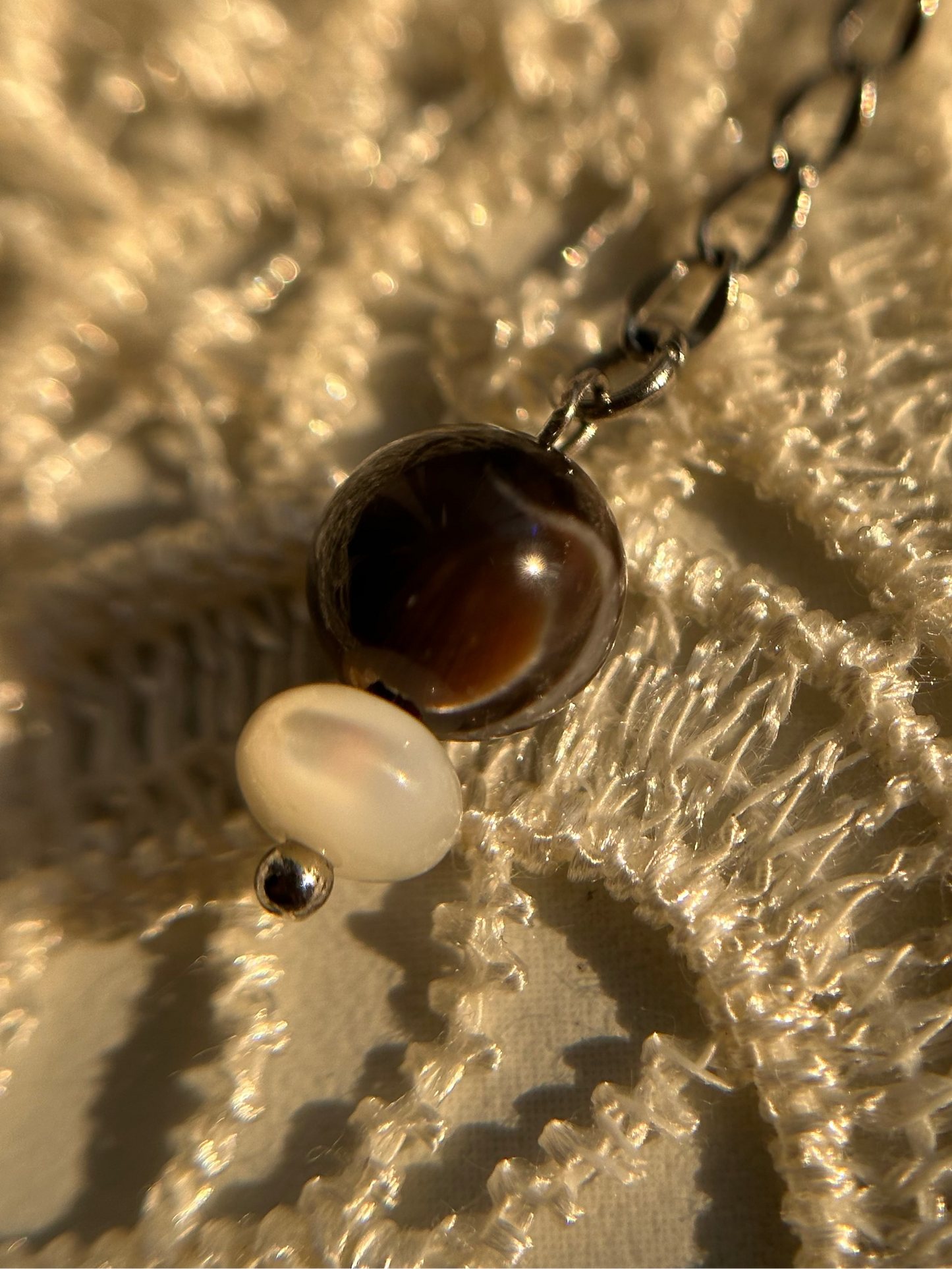 Necklace with a brown and white bead on a textured beige surface