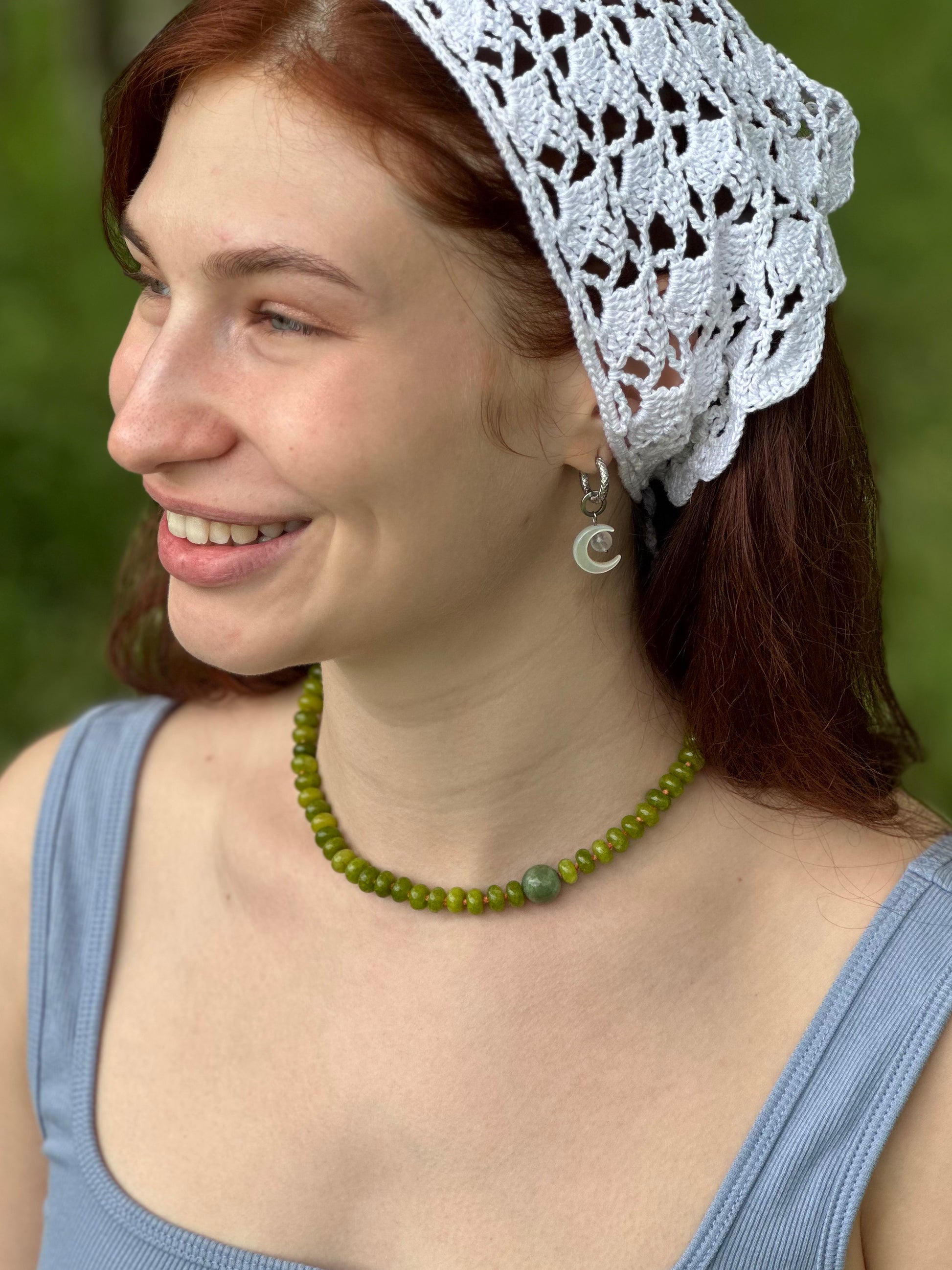 Woman wearing a white lace headscarf and green beaded necklace against a blurred green background