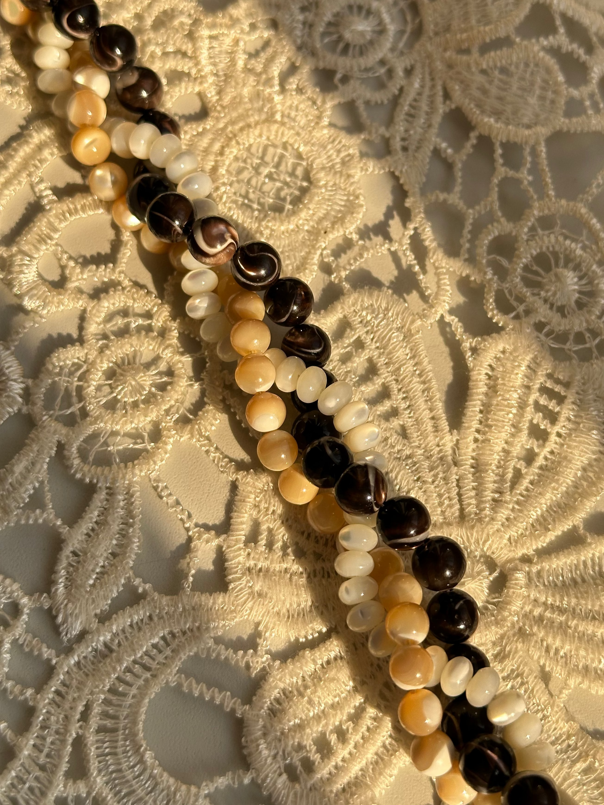Necklace with black, white, and beige beads on a lace background