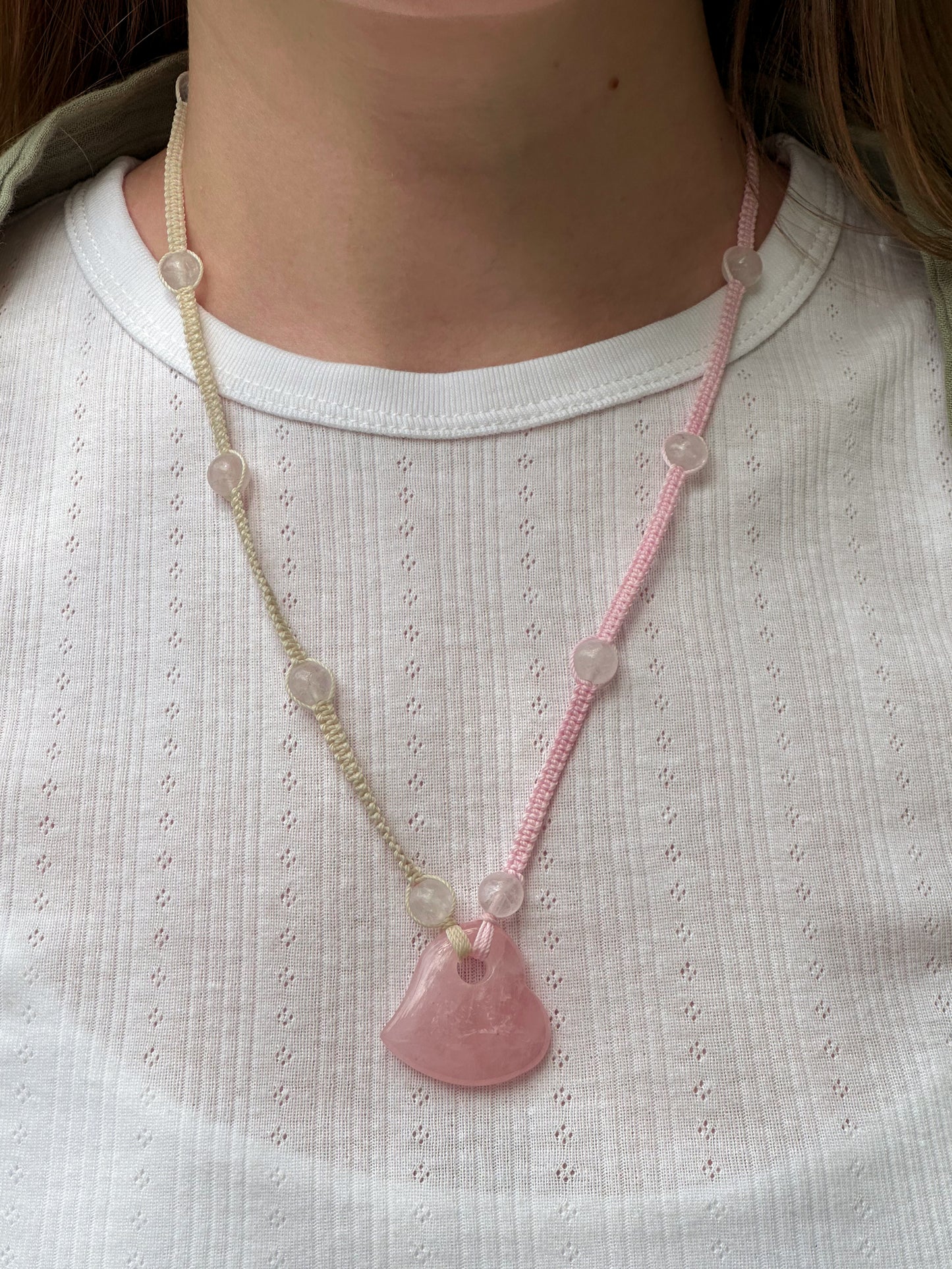Necklace with a pink pendant worn by a person on a white shirt