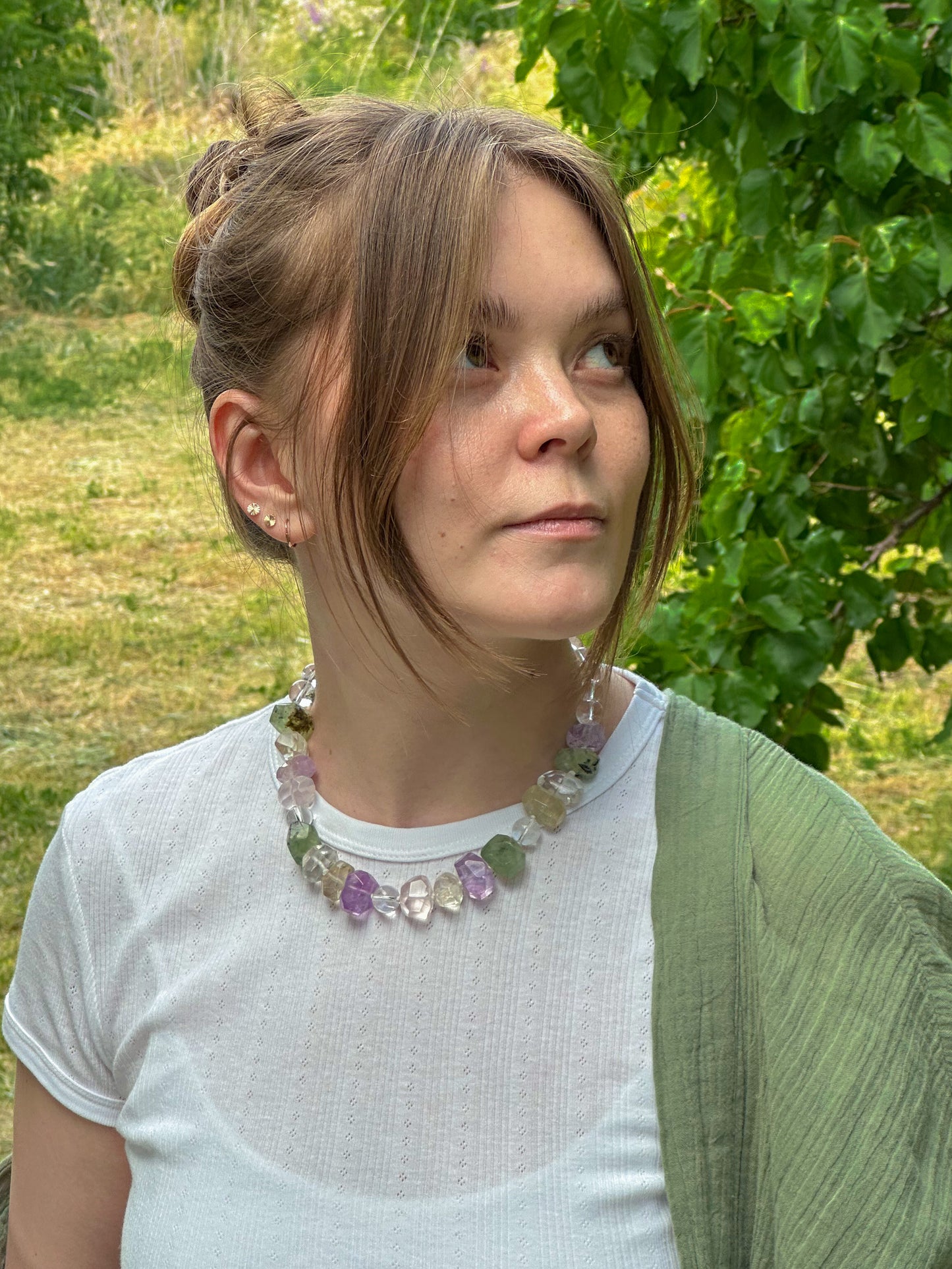 Woman wearing a colorful necklace outdoors with greenery in the background