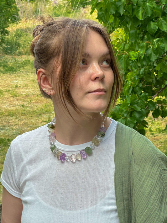 Woman wearing a colorful necklace outdoors with greenery in the background