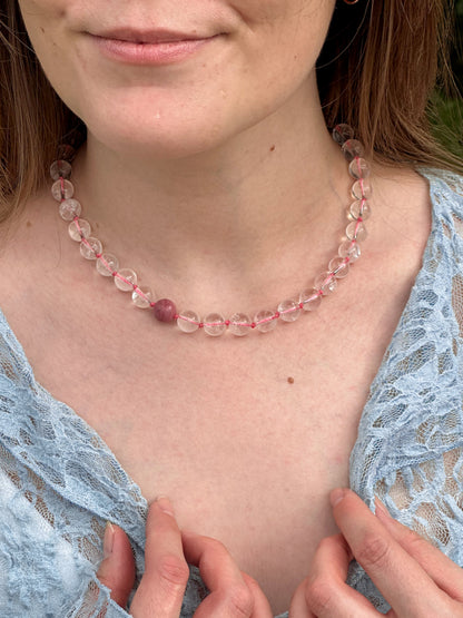 Woman wearing a pink beaded necklace with a blue lace top.