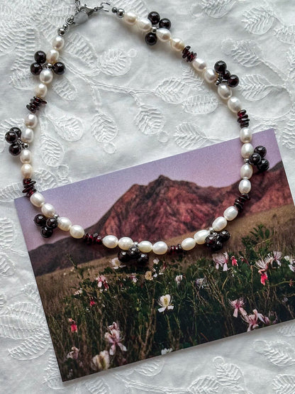 Necklace with pearls and dark beads on a scenic card with mountains and flowers
