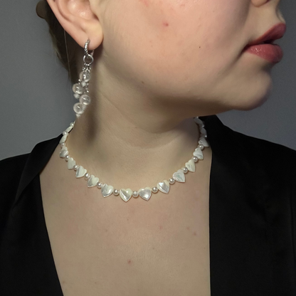 Close-up of a person wearing a pearl necklace and earrings against a neutral background
