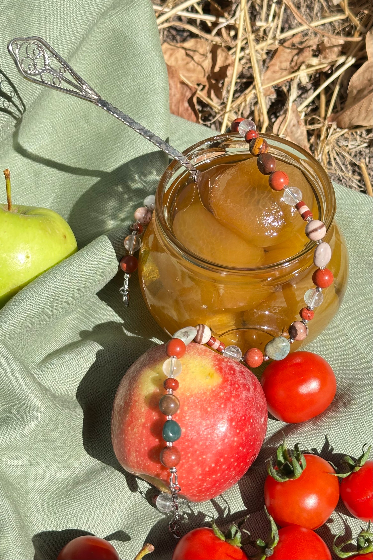 Jar of honey with a honeycomb on a green cloth with apples and tomatoes.