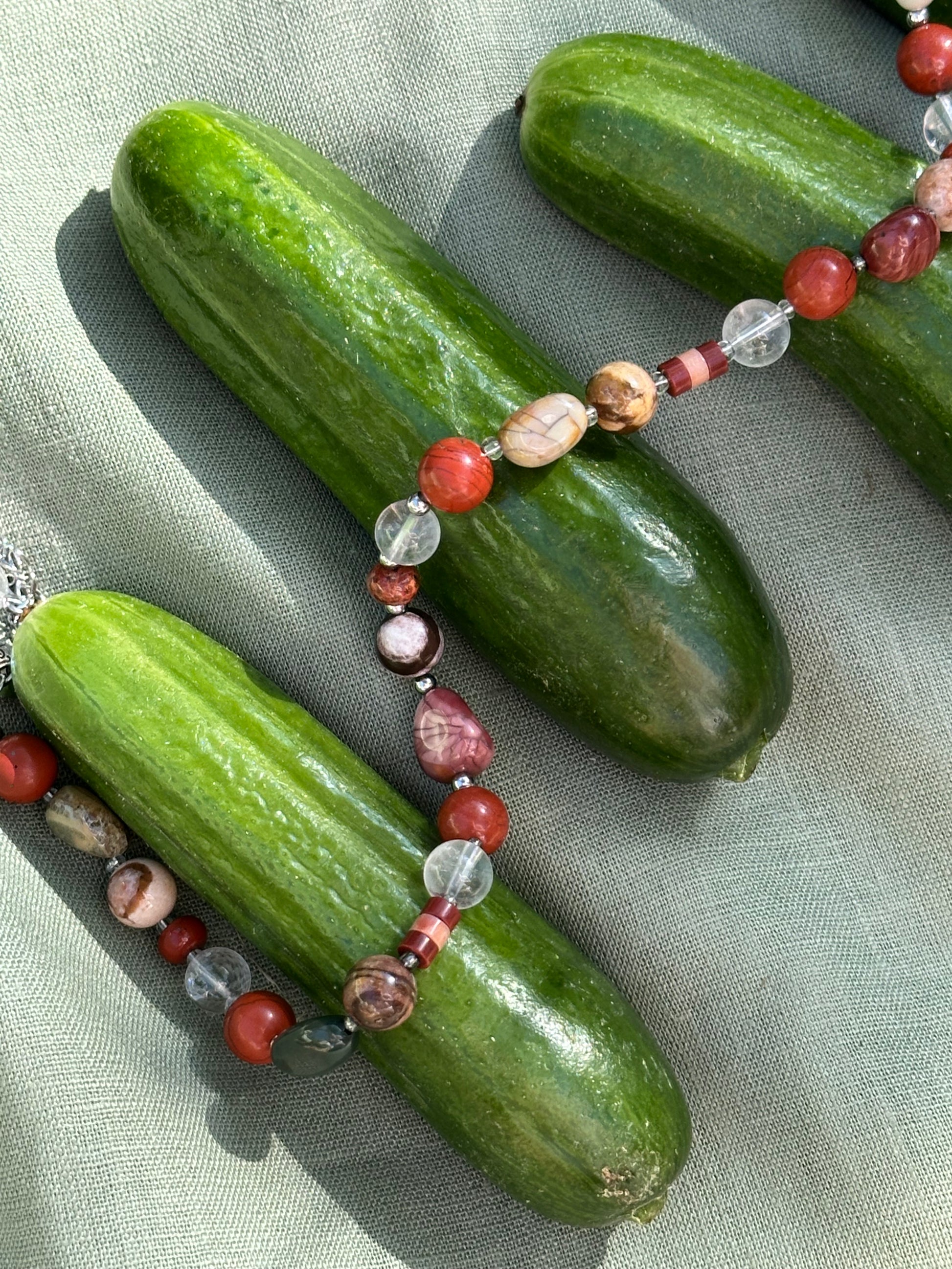 Green cucumbers with a beaded necklace on a light fabric background