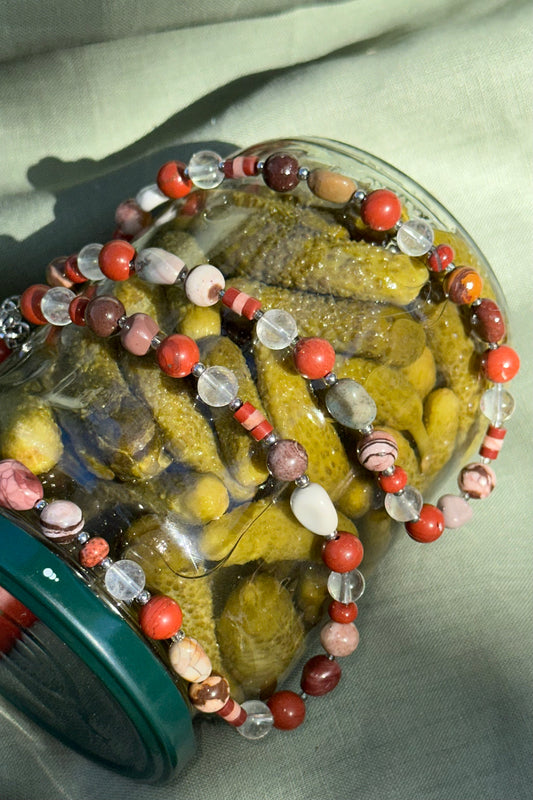 Jar of pickles with a decorative bead necklace on a light fabric background
