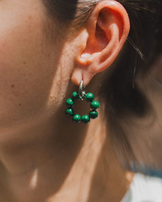 Close-up of an ear wearing a green beaded earring with blurred background