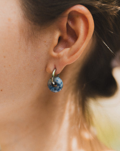 Close-up of an ear wearing a blue speckled earring with a blurred background