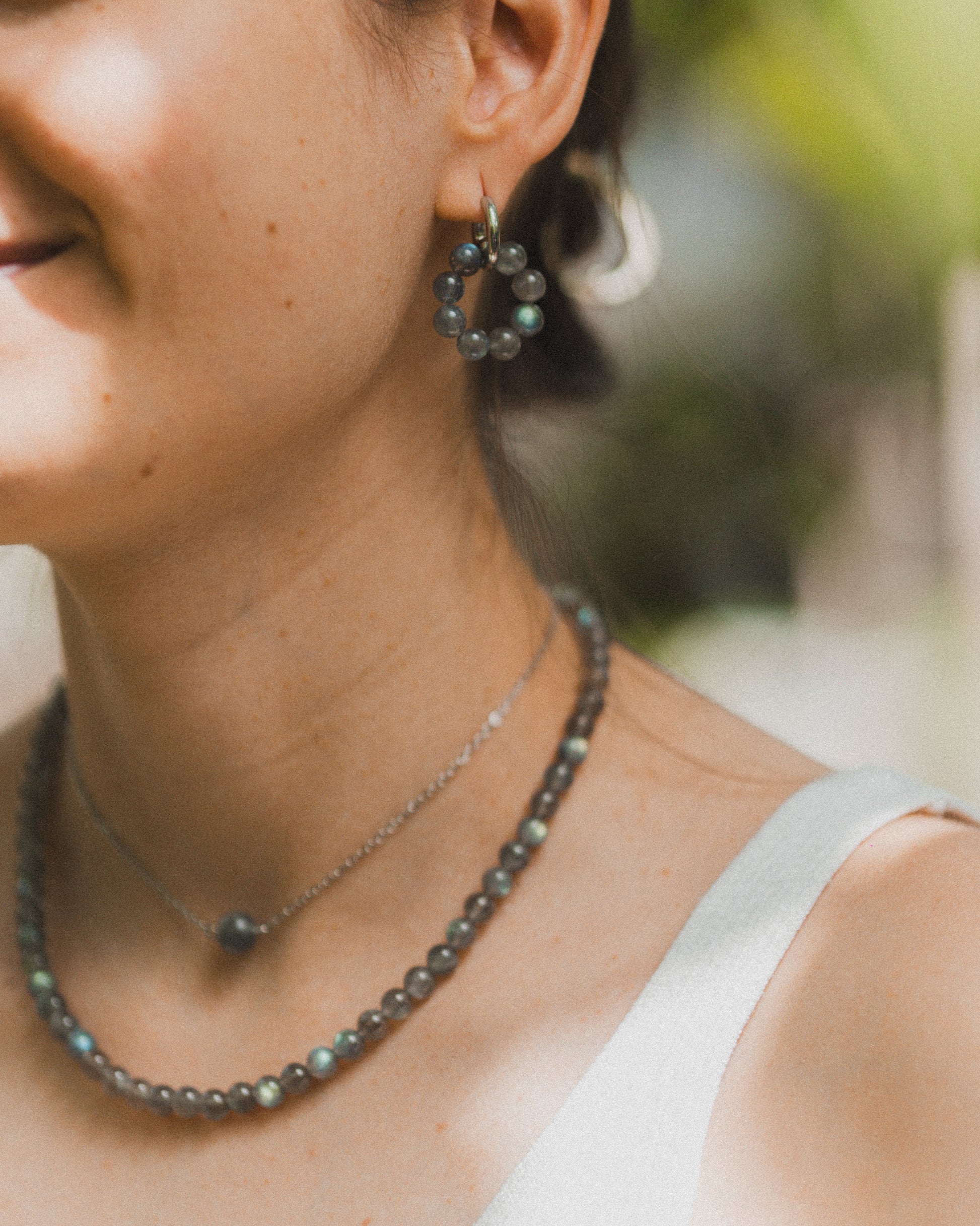 Close-up of a woman wearing earrings and a necklace with a blurred natural background