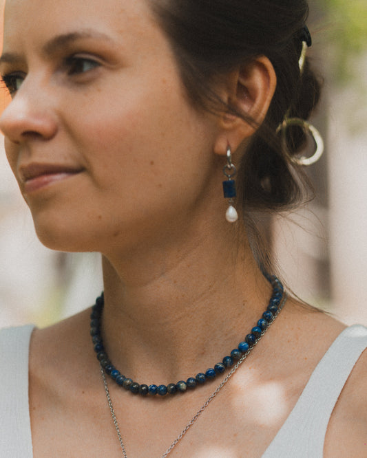 Woman wearing a blue beaded necklace and earrings with a blurred background