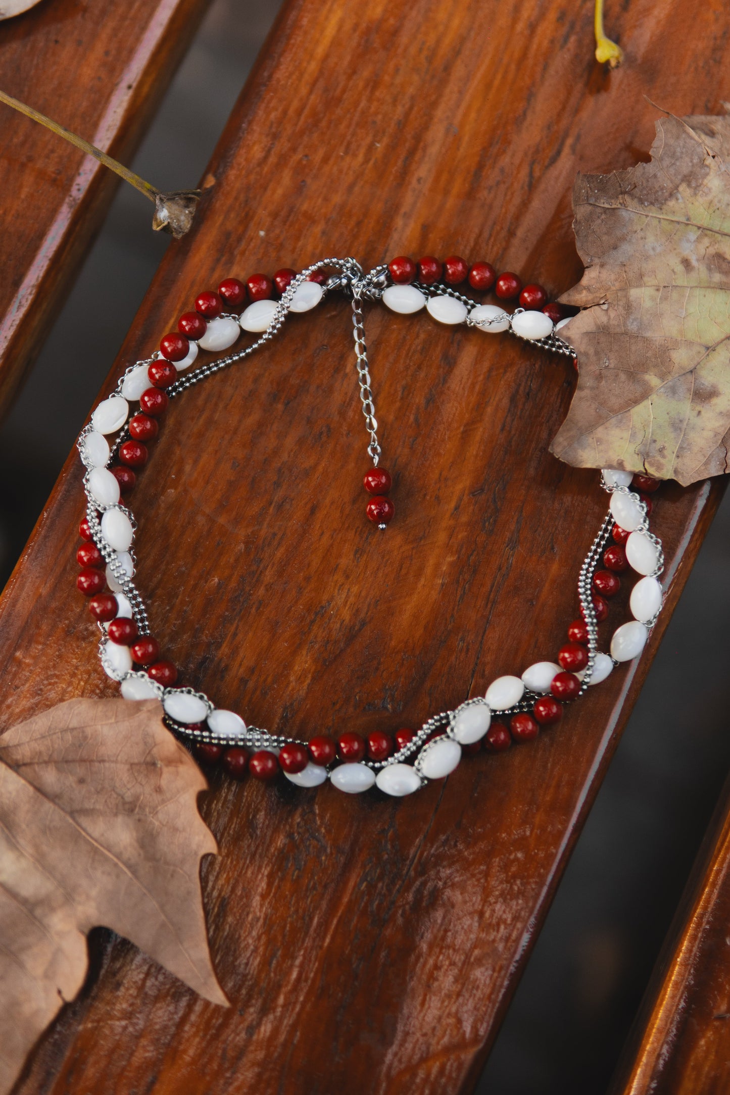 Beaded bracelet with red and white beads on a wooden surface with leaves.