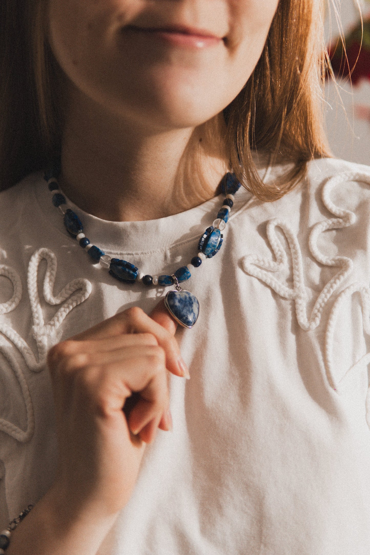 Person wearing a white embroidered top and blue beaded necklace.