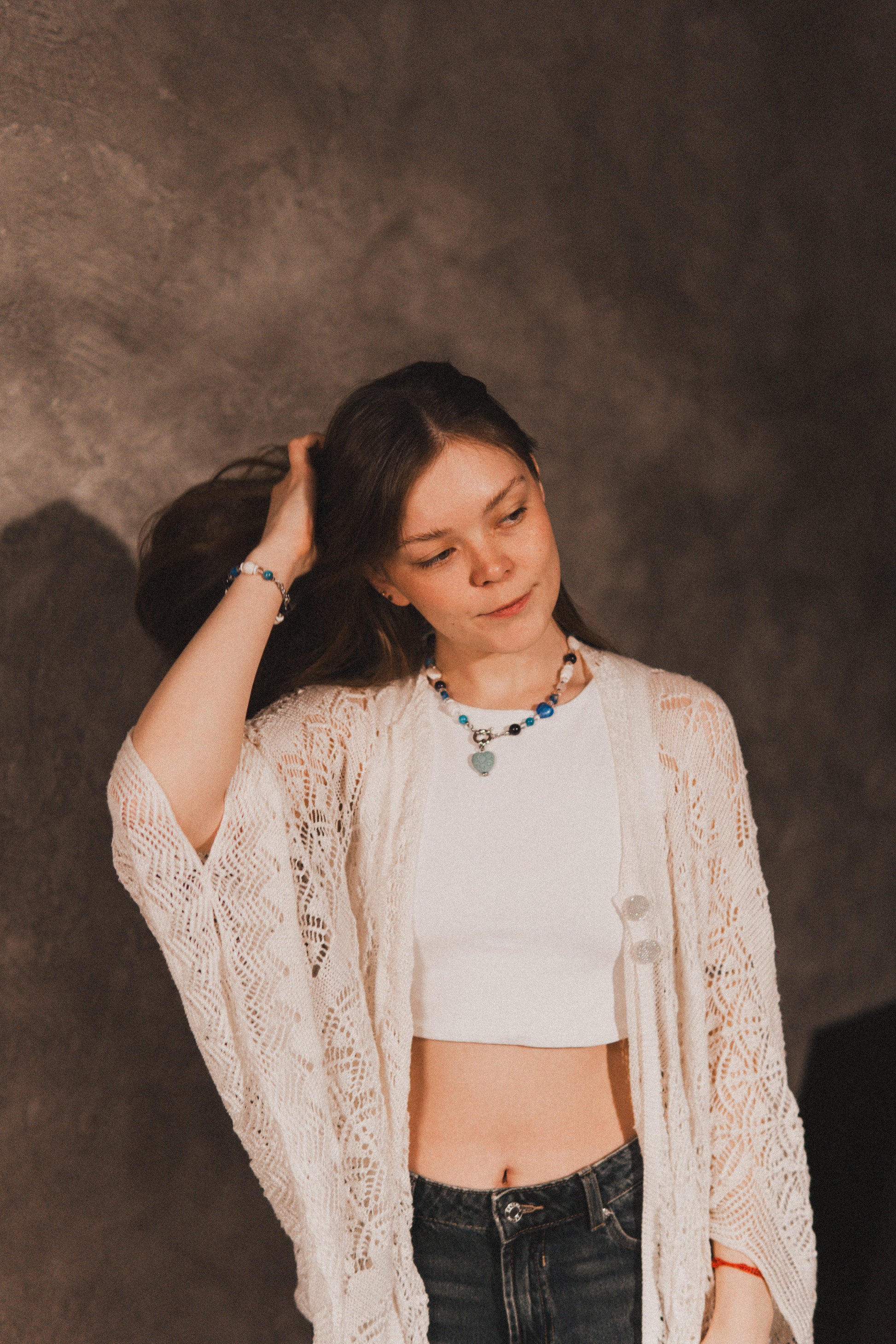 Woman wearing a white crop top and beige cardigan against a dark background