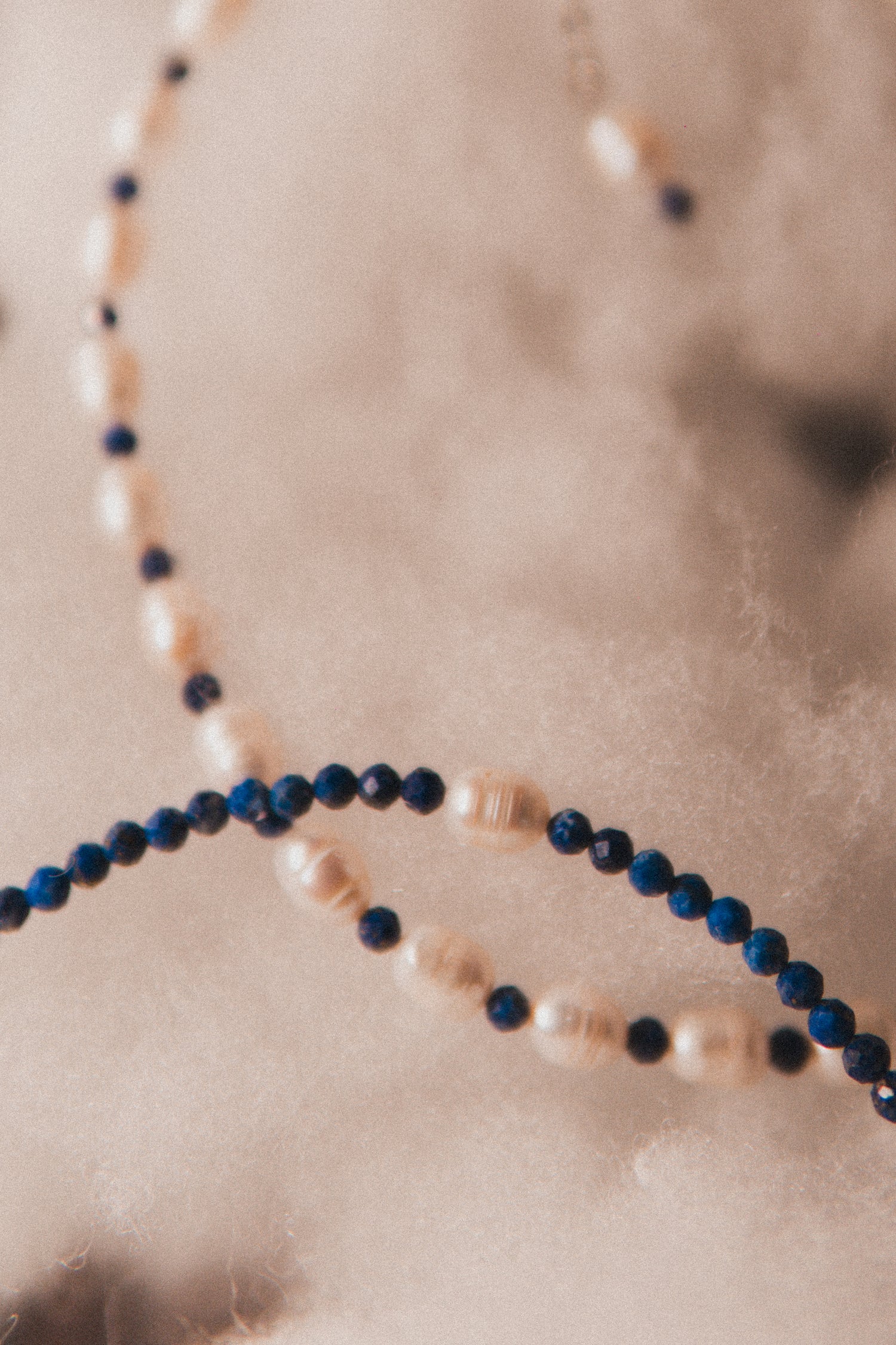 Close-up of a necklace with blue and beige beads on a neutral background