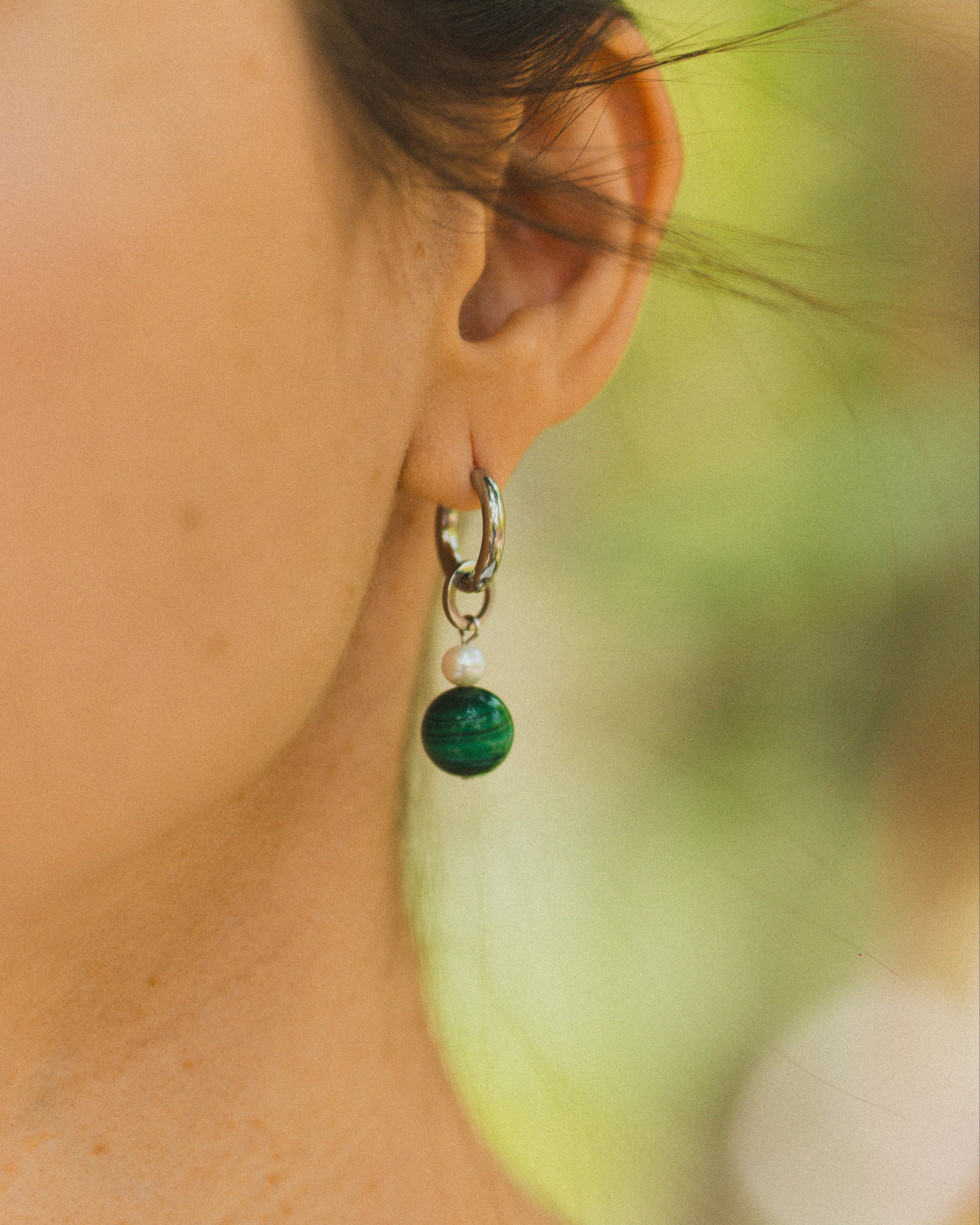 Close-up of a person wearing a green bead earring with a blurred natural background
