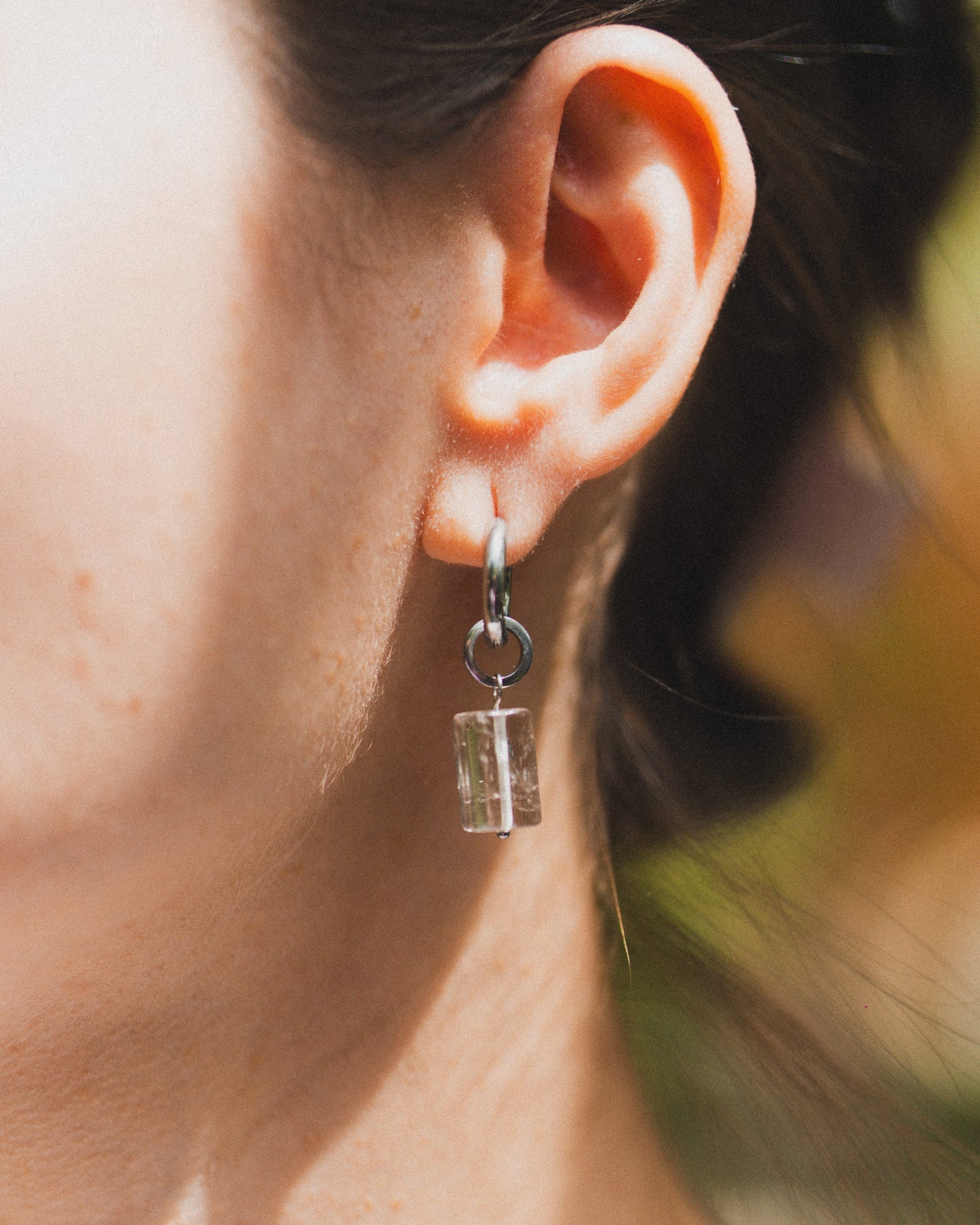 Close-up of an ear wearing a silver earring with a small pendant.