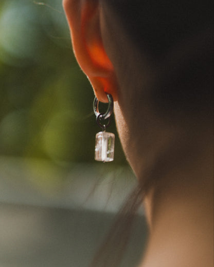 Close-up of a person wearing an earring with a clear gemstone against a blurred natural background