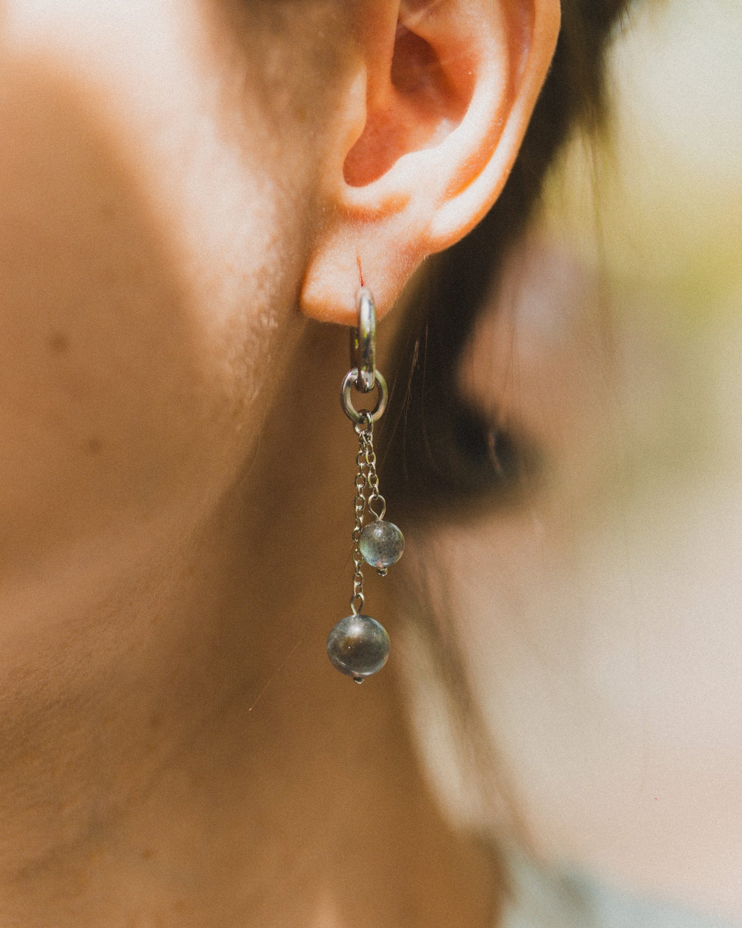 Close-up of an ear wearing a dangling earring with a blurred background