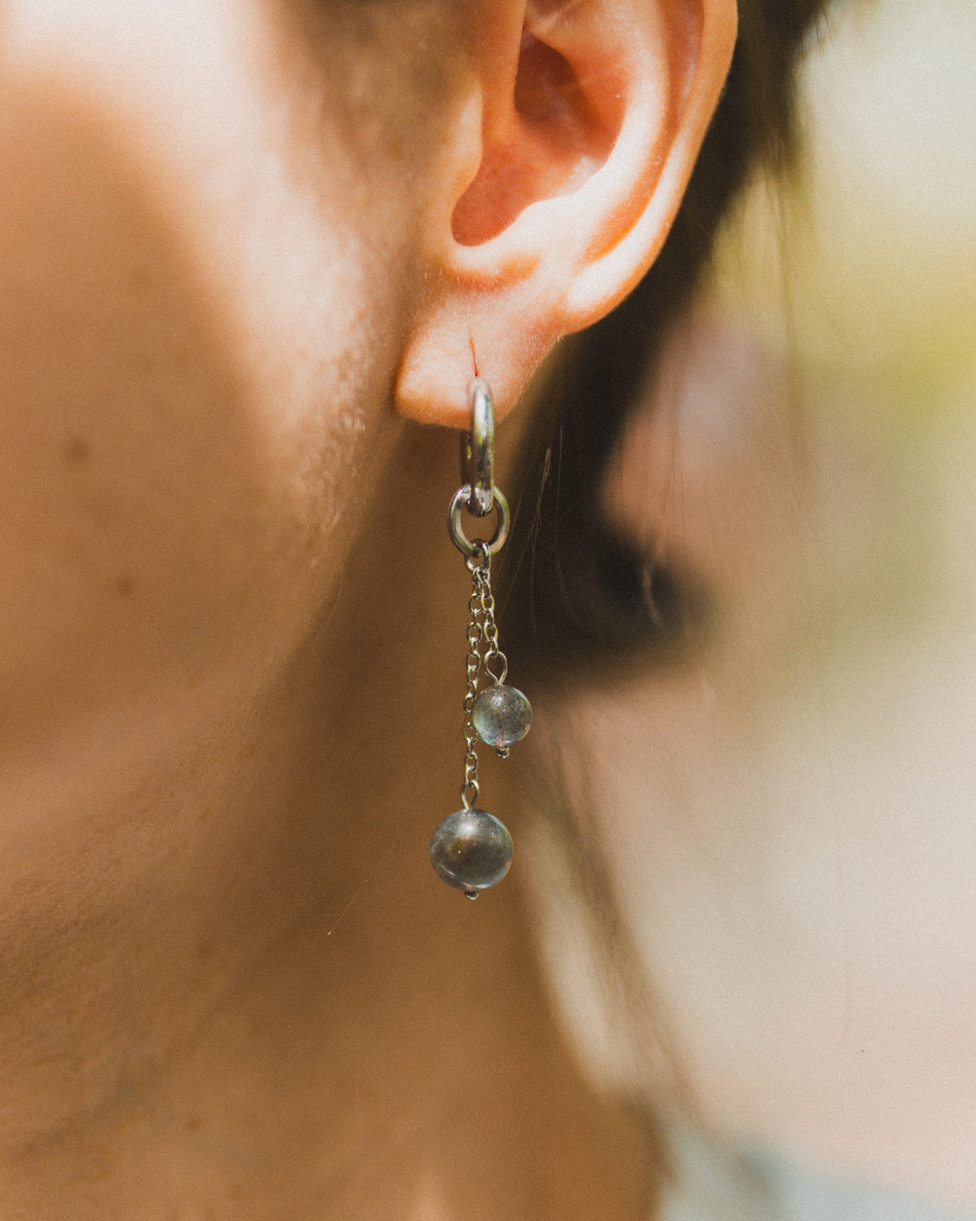 Close-up of an ear wearing a dangling earring with a blurred background