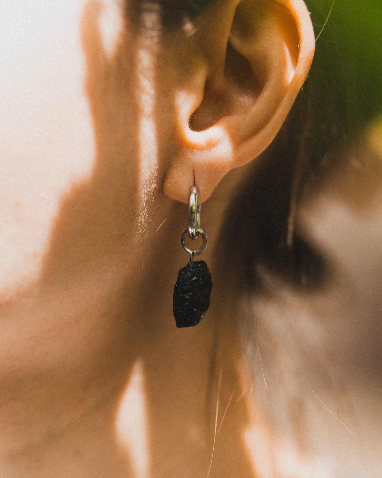 Close-up of an ear wearing a black stone earring with a blurred background