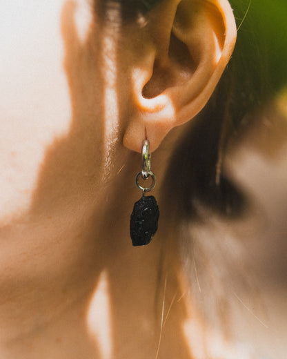 Close-up of an ear wearing a black stone earring with a blurred background