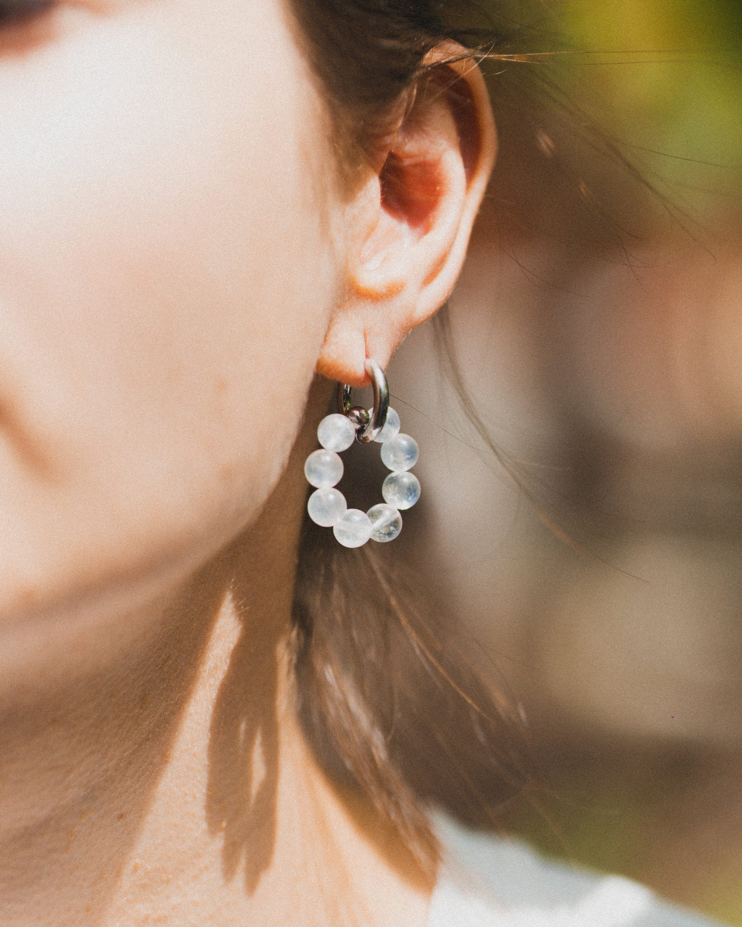 Close-up of a person wearing a circular earring with clear stones against a blurred natural background