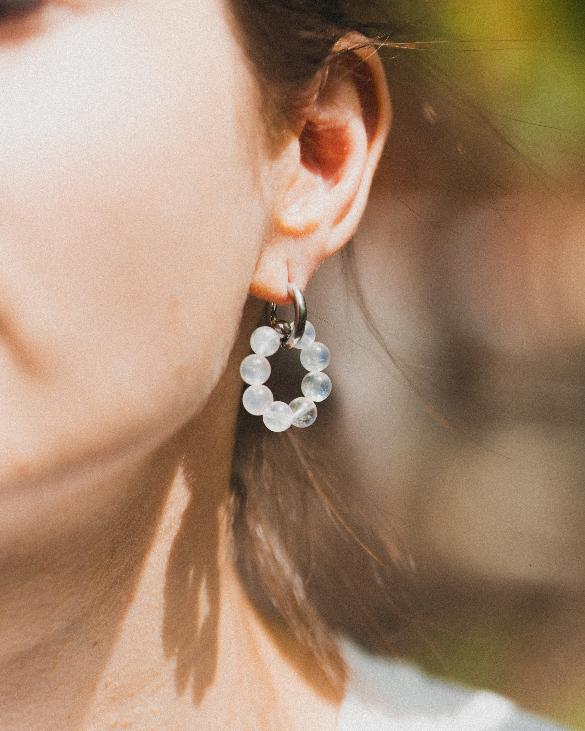 Close-up of a person wearing a circular earring with clear stones against a blurred natural background